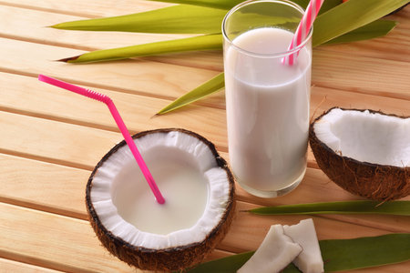 Coconut milk in containers with coconut fruit on wooden table. Alternative milk concept. Elevated...