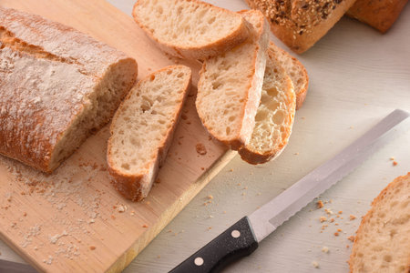 Loaf of bread cut into slices on cutting board on the bench of a kitchen. Top view. Horizontal...