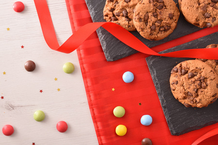 Celebration with chocolate cookies on slate tray on white table with red tablecloth decorated with ribbon and sweets. Top view. Horizontal compositionの写真素材