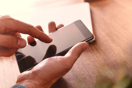 Hands of a man touching a telephone on a brown wooden table. Horizontal composition