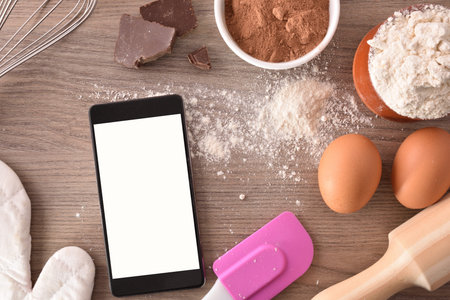Pastry ingredients on a wooden table with mobile. Concept of recipes in digital book. Horizontal...