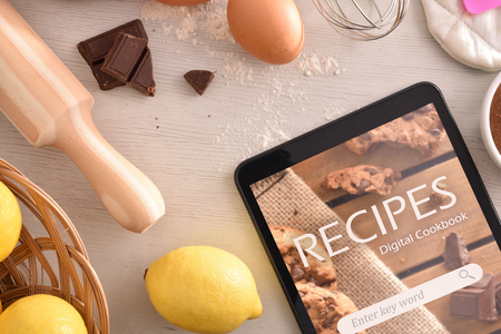Tablet with online recipes app and pastry ingredients background. Use of the digital devices to cook. Concept of recipes in digital book. Horizontal composition. Top viewの写真素材
