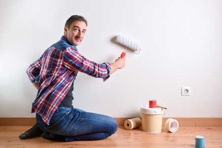Smiling man kneeling on a parquet floor with paint material painting his house. Front view. Horizontal composition.の写真素材