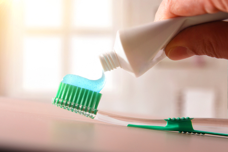 Concept oral hygiene with hand putting toothpaste on toothbrush on wood table in bathroom. Horizontal composition. Front view.の写真素材