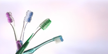 Four colorful transparent tooth brushes on pink and blue gradient background fan-shaped. Horizontal composition.の写真素材
