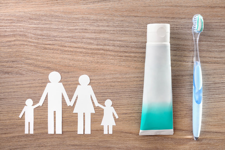 Concept of teeth cleaning at home of the whole family with glass jar with toothbrushes and family cutout on wooden table . Horizontal composition. Top viewの写真素材