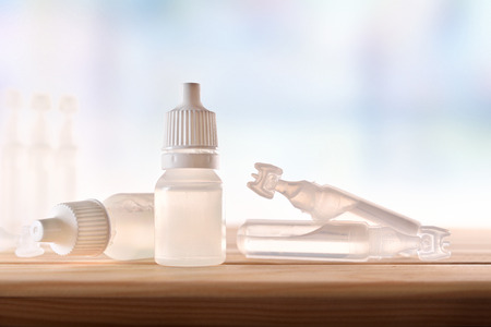 Plastic bottle with eye medication on wooden table in room. Horizontal composition. Front view.の写真素材