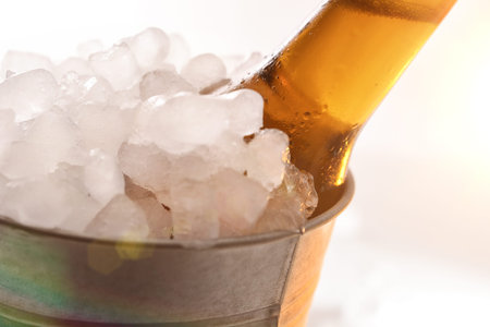 Beer bottle in metal bucket full of ice cubes close up. Horizontal composition. Front view.