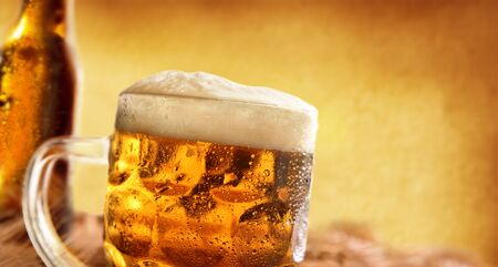 Pitcher full of beer with foam and bottle behind on wooden table decorated with barley ears with toasted brown gradient background. Horizontal composition. Front view.の写真素材
