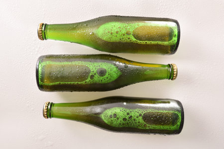 Three green bottles with alcoholic beverage on white table. Horizontal composition. Top view.