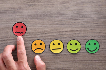Hand pointing a level of negative satisfaction represented with colored emoticons on wood table....
