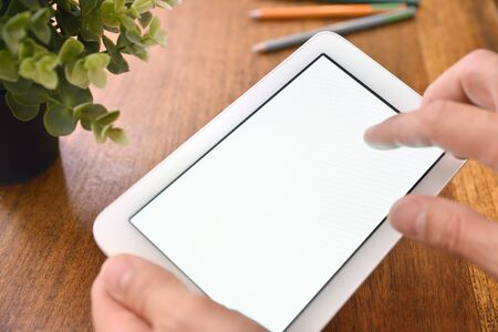 Hands using white tablet with white screen on desk close up. Horizontal composition. Elevated viewの写真素材