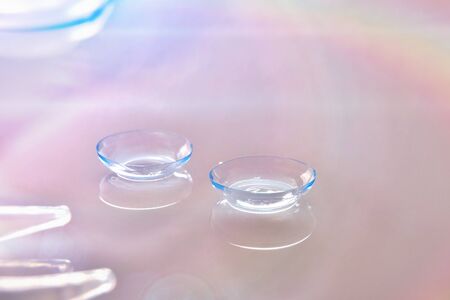 Contact lenses on white reflective glass table with reflection of colored lights. Horizontal composition. Elevated viewの写真素材