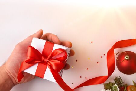 hand with gift and christmas background with ball and ribbon and floral motif on white table. Horizontal composition. Top view.の写真素材