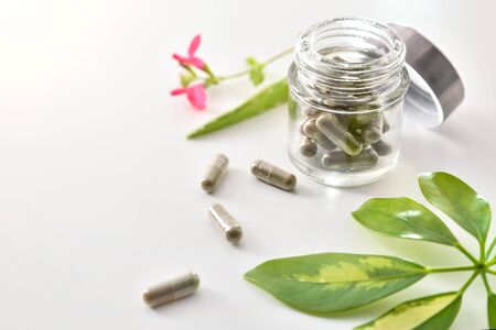 Natural medicine capsules in open glass jar lying on white table with aloe vera and plant leaves. Natural medicine concept. Elevated view. Horizontal composition.の写真素材