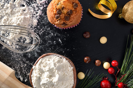 Background with elaboration of muffins for the christmas holidays on black table with ingredients...