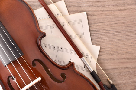 Violin body and bow with sheet music on wood table. Top view. Horizontal composition.