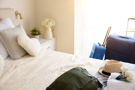 Bright and sunny vacation hotel room with suitcases and hand luggage and straw hat on the bed.
