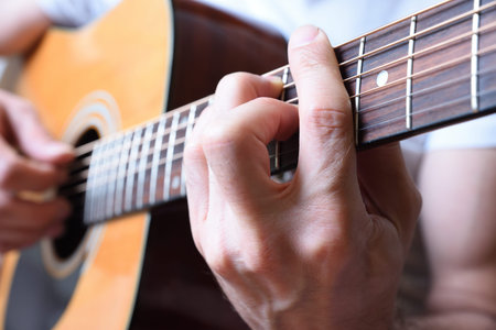 Detail of man playing acoustic guitar with hand making chord