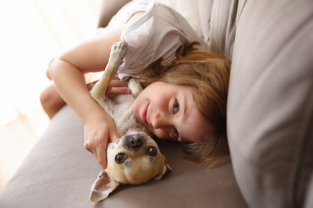 Smiling girl lying with her dog on the sofa looking at cameraの写真素材