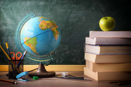 Stack of books and school supplies on classroom desk with green blackboard backgroundの写真素材