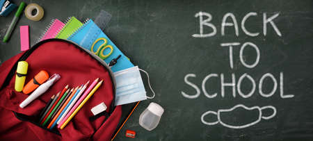 Backpack full of school supplies on green blackboard with protection mask and hydroalcoholic gel with back to school message and mask design. Top View.の写真素材