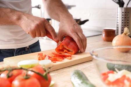 Hands of a casual man cutting a bell pepper on cutting board on the kitchen bench with vegetables aroundの写真素材