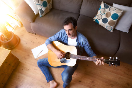 Man composing for guitar sitting on the floor in the living room at home. Top view.