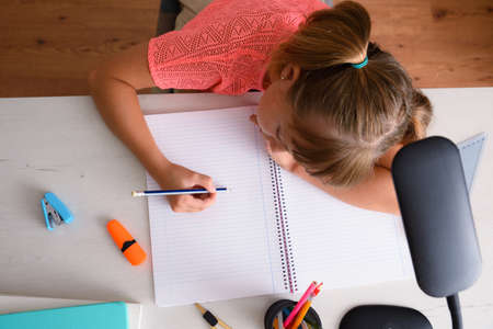Little girl studying on desk with school supplies writing in notebook. Top view.の写真素材