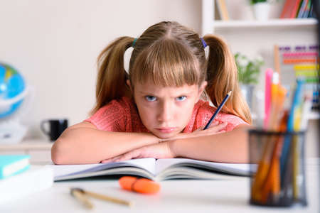 Little girl studying at home angry with crossed arms over book at study desk at homeの写真素材