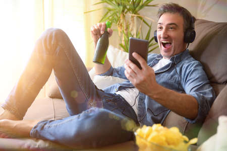 Man having a snack at home fun listening to music with headphones from a mobileの写真素材