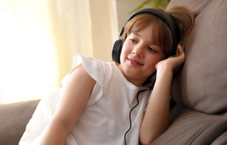 Girl with helmets listening to music sitting on the sofa at home in a quiet and warm environmentの写真素材