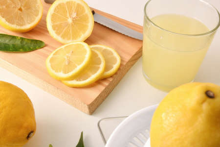Lemon slices on cutting board and squeezed lemon in glass vase on white table. Elevated view. Horizontal composition.の写真素材