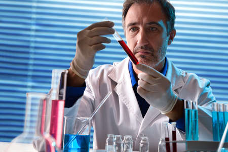 Biochemist in laboratory looking at a sample in a test tube. Horizontal composition. Front view.の写真素材