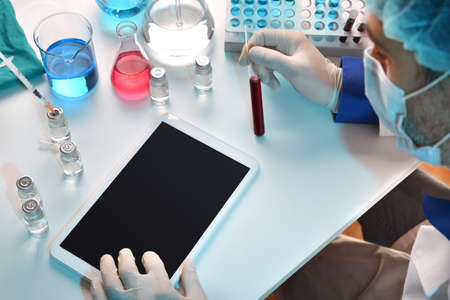 Lab worker using tablet with blood sample on workbench with vials and supplies. Horizontal composition. Top elevated view.の写真素材