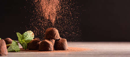 Chocolate truffles with mint leaves on wooden table and dark background falling cocoa powder. Front view. Horizontal panoramic composition.の写真素材