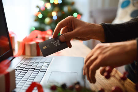 Concept of person doing christmas shopping online at home from a laptop  with card. Front view. Horizontal composition.の写真素材