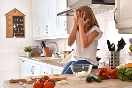 Little girl sitting on kitchen bench preparing food with hands on face at homeの写真素材
