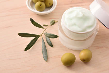 Moisturizing cosmetic cream with olive extract for skin with branch and olives on wooden table. Elevated view.の写真素材