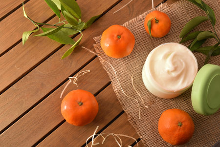 Natural tangerine cosmetic cream on wooden table with fruit and leaves. Top view.