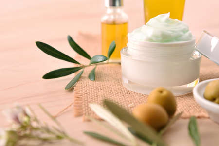Moisturizing cosmetic cream with olive extract for skin and serum with branch and olives on wood table. Elevated view.の写真素材