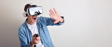 Modern adult man interacting with virtual reality glasses controlling with a joystic with light...