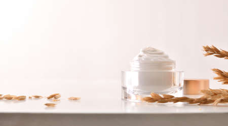 Oat body and facial moisturizer cream in glass jar with spikes on wooden table with white isolated backgroundの写真素材
