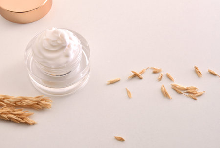 Oat body and facial moisturizer cream in glass jar with spikes on wooden table with white isolated...