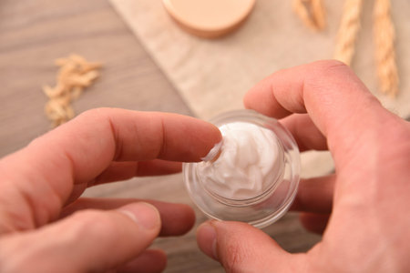 Hands taking natural moisturizing cream of oat extract for application with wooden table background...
