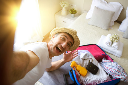 Happy man on vacation taking a selfie with hat on her head in a hotel room