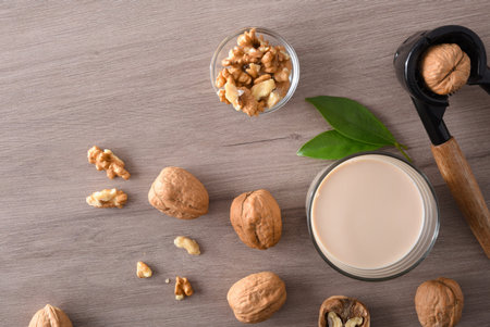 Glass full of vegetable milk of walnuts with fruits around on and wooden table with nutcracker. Top...