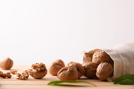 Group of walnuts spilling out of a cloth sack and seeds and leaves on wooden table. Front view.