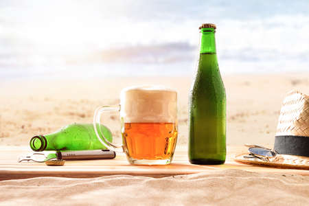 Bottle and mug of fresh beer on the sand at the beach. Front view detail.の写真素材