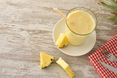 Glass with pineapple and milk shake and pineapple portions on wooden table with pineapples around....